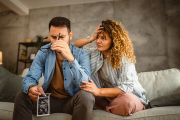 Naklejka premium Stress couple sit and talk about ultrasound picture of unwanted baby