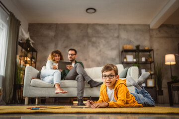 Young boy child draw and lies on the carpet while parents use tablet