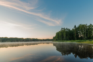 Small forest lake covered with fog at sunrise on June morning