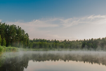 Small forest lake covered with fog at sunrise on June morning