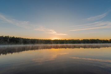 Small forest lake covered with fog at sunrise on June morning