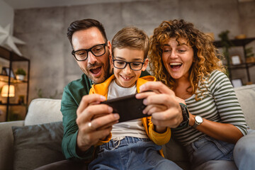 mum, dad and son play video games together on mobile phone at home