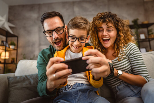 mum, dad and son play video games together on mobile phone at home - Powered by Adobe