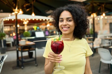Young latin woman holding a drink at an outdoor terrace