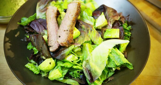 Adding grilled steak pieces onto red romaine salad