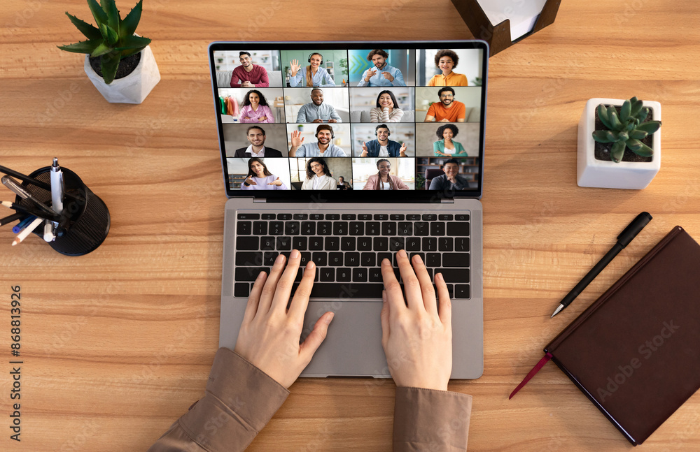 Poster A person is participating in a video conference using a laptop computer. The screen shows multiple people in a grid format. The persons hands are on the keyboard of the laptop, top view
