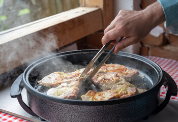 Summer kitchen in the countryside. A man's hand turns pork or beef in a large special pan for frying and stewing meat.