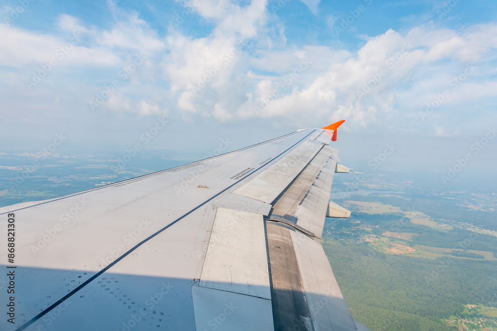 Wall mural View of airplane wing, blue skies and green land during landing. Airplane window view.