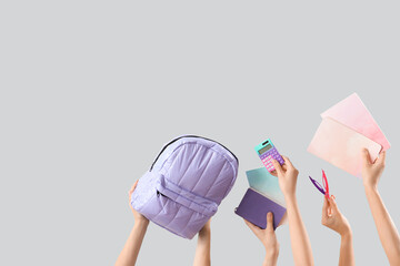 Many female hands with backpack and different stationery on grey background