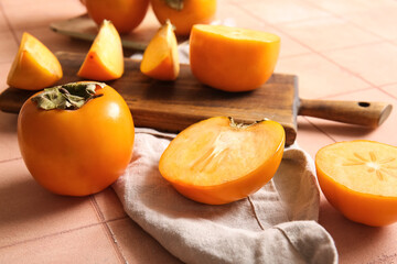 Wooden board with sweet ripe persimmons on pink tile background
