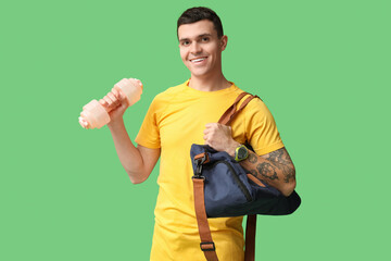 Young man with sports bag and dumbbell on green background