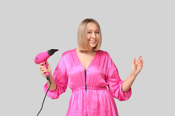 Happy young woman with bob hairstyle holding hair dryer on grey background