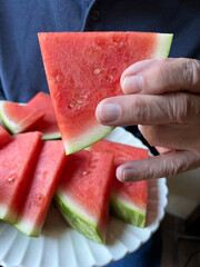 Man holds watermelon piece from platter of slices
