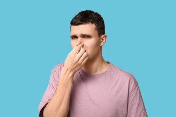 Handsome young man pinching nose because of bad smell on blue background