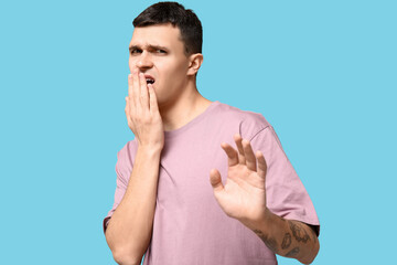 Handsome young man feeling bad smell from mouth on blue background