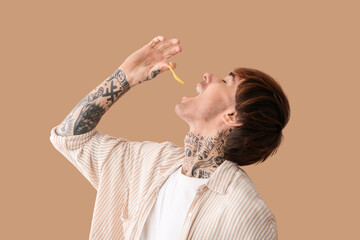Young tattooed man eating potato chips on beige background