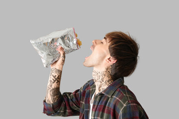 Young tattooed man eating potato chips on light background