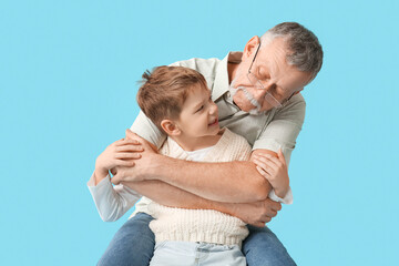 Grandfather hugging his happy cute little grandson hugging on blue background