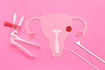 Paper uterus with gynecological speculum and pap smear test tools on pink background