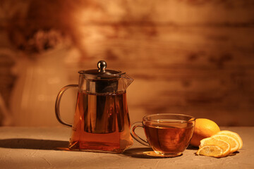 Composition of glass teapot, slices of lemon and cup with tea on wooden table against blurred background