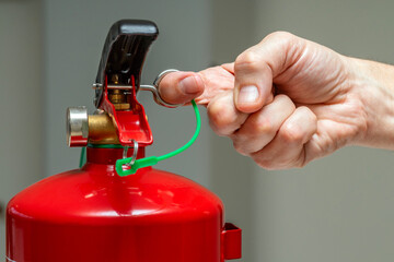 Close up of a hand pulling the safety pin of a fire extinguisher. Fire protection systems.
