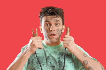 Electrocuted young man with burnt face and jumper cables on red background, closeup