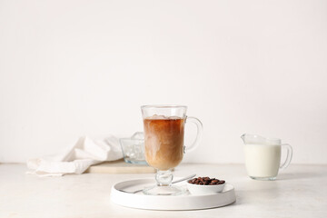 Glass cup of iced latte, bowl with coffee beans and jug of milk on white background