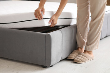Young woman putting soft mattress on bed in bedroom, closeup