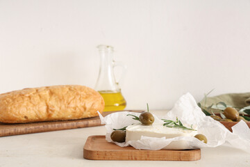Wooden board with tasty feta cheese, olives and rosemary on white background