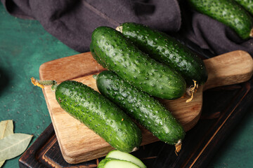 Wooden board with fresh cucumbers on green background