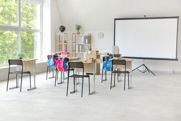 Interior of light classroom with projector screen and desks