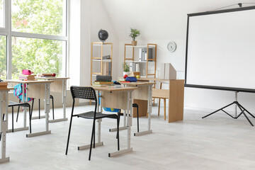 Interior of light classroom with projector screen and desks