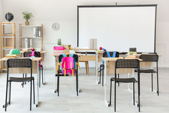 Interior of light classroom with projector screen and desks