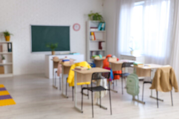 Blurred view of classroom with chalkboard, desks and shelf units