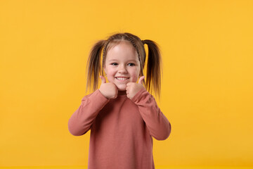 Cute little girl showing thumbs up on orange background