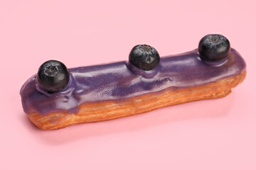 Delicious eclair decorated with blueberries on pink background