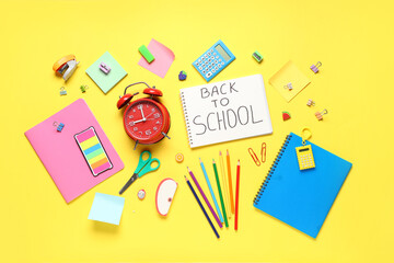 Alarm clock, notebook with text BACK TO SCHOOL and different stationery on yellow background
