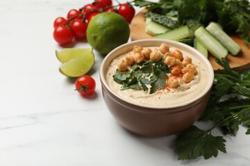 Tasty hummus with chickpeas in bowl and fresh products on light table