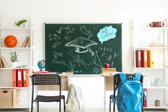 Interior of empty classroom with blackboard, shelf units and desks