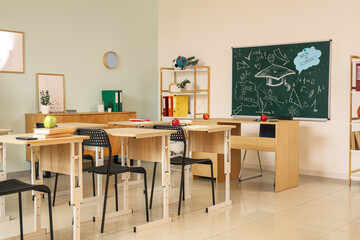Interior of empty classroom with blackboard, shelf unit and desks
