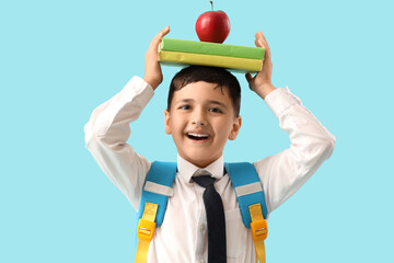 Little schoolboy with apple and books on blue background