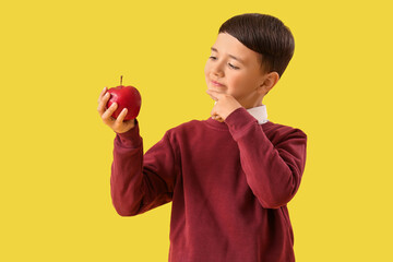 Thoughtful little schoolboy with apple on yellow background