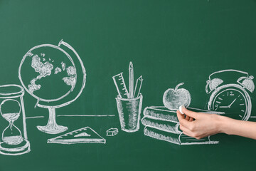 Female hand drawing school supplies on green chalkboard