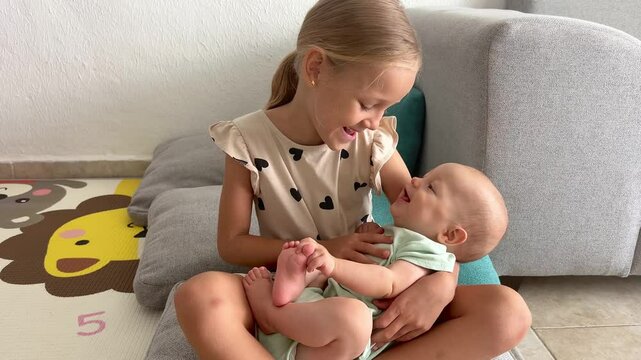 The older preschooler sister holds her younger sister in her arms and entertains her. Concept of family life, relatives and childhood.