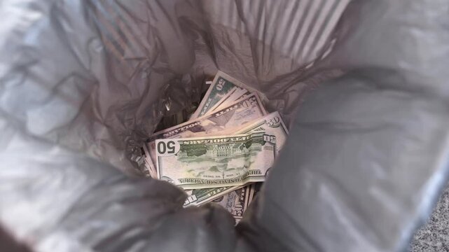 Close-up of a pack of fifty bills being thrown into an office trash bin, trash bag. Concept of wasting money, inflation, loss of savings on investments Wasting money, squandering, financial losses