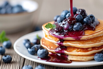 Delicious stack of fluffy pancakes topped with fresh blueberries and drizzled with rich blueberry syrup.