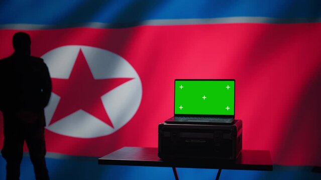North Korea secret police agent uses mass propaganda tools on green screen laptop to influence population minds. Pyongyang regime commits PsyOp sabotage using mockup device, camera B