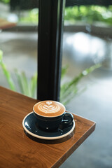 A cup of coffee with heart-shaped latte art on a wooden table with bokeh background. Portrait or vertical shot.