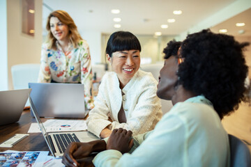 Multiethnic female colleagues discussing work with laptops in a modern office