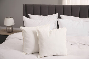 Many soft white pillows and duvet on bed indoors